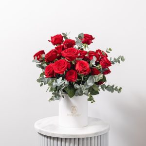 A luxurious red rose and eucalyptus arrangement in a box.