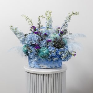 A stunning flower basket of fresh blue blooms with natural feathers and delicate foliage.