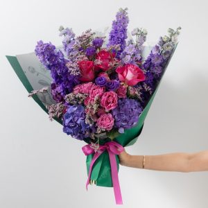 A stunning bouquet of fresh purple flowers, including delphiniums, hydrangeas, and roses.