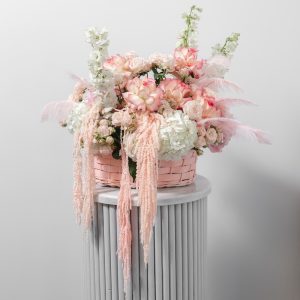 A stunning flower basket with soft pink and white blooms, real feathers, and preserved amaranthus.