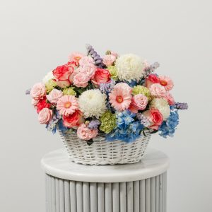 A beautiful, mixed-color flower basket with blue hydrangeas, white peonies, and pink gerberas.