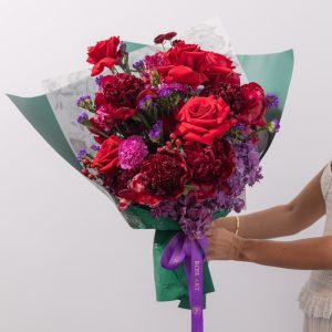 A luxurious bouquet of deep red and dark purple flowers, including red peonies, roses, and hydrangeas.