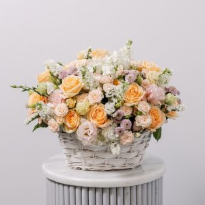 A hand-tied flower basket with a mix of fresh pastel blooms, including peach gerberas, hydrangeas, and roses.
