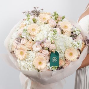 A large, beautiful bouquet of fresh pastel flowers, including a peach gerbera, roses, and hydrangeas.