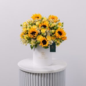 A cheerful flower box arrangement with fresh sunflowers, yellow roses, and white chamomile.