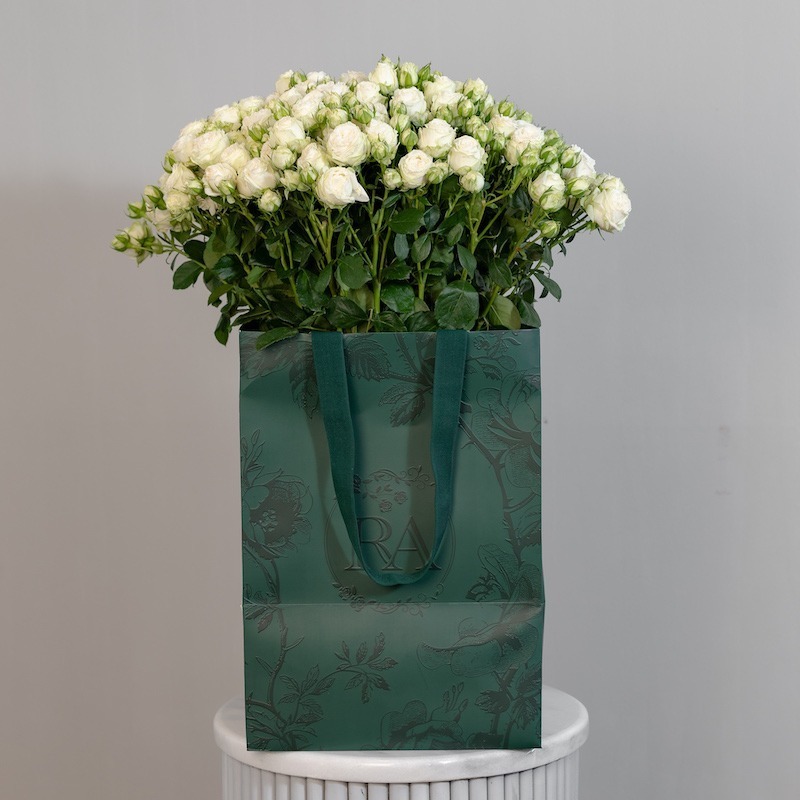 A large bunch of Miss Bombastic spray roses arranged in a tall, elegant glass vase, ready to be displayed in a home or office setting.