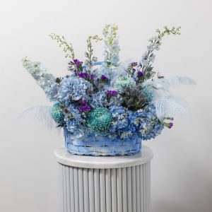 A stunning flower basket of fresh blue blooms with natural feathers and delicate foliage.