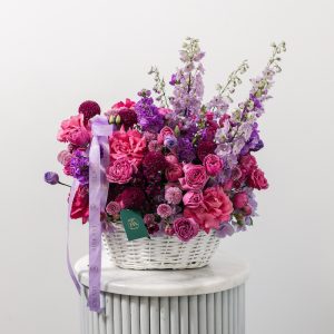 A stunning basket arrangement of fresh purple flowers, including delphiniums, hydrangeas, and roses.