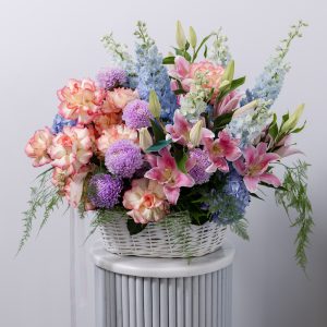 A beautiful flower basket filled with vivid pink, purple, and blue blooms, including lilies, chrysanthemums, and hydrangeas.