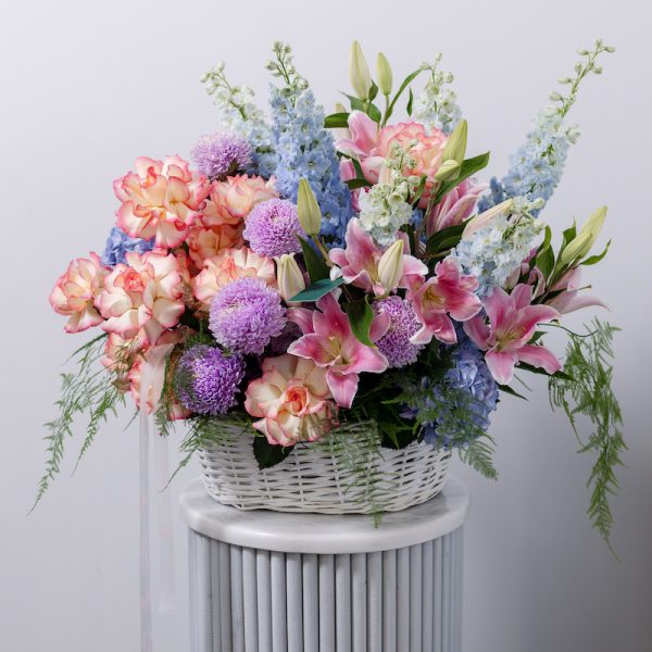 A beautiful flower basket filled with vivid pink, purple, and blue blooms, including lilies, chrysanthemums, and hydrangeas.