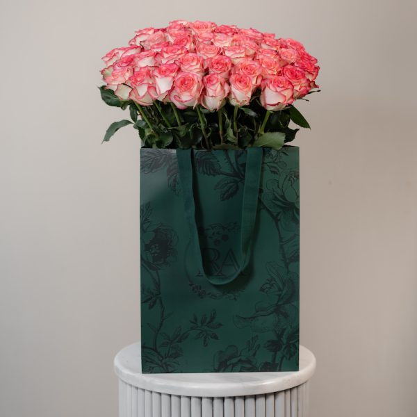 A large bunch of Jumilia roses arranged in a tall, elegant glass vase.
