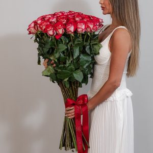A large bunch of pink and white roses arranged in a tall, elegant glass vase.