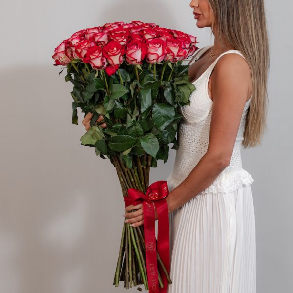 A large bunch of pink and white roses arranged in a tall, elegant glass vase.