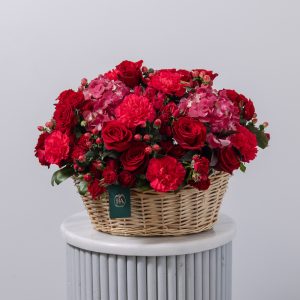 A large, beautiful floral basket with a mix of red and dark pink flowers, including roses and hydrangeas.