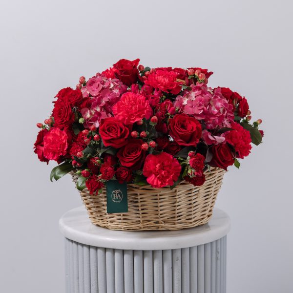 A large, beautiful floral basket with a mix of red and dark pink flowers, including roses and hydrangeas.
