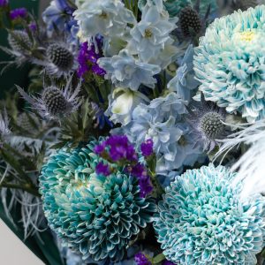 A close-up side view of the Art of Blue bouquet, showing the detail of the blue flowers and feather accents.