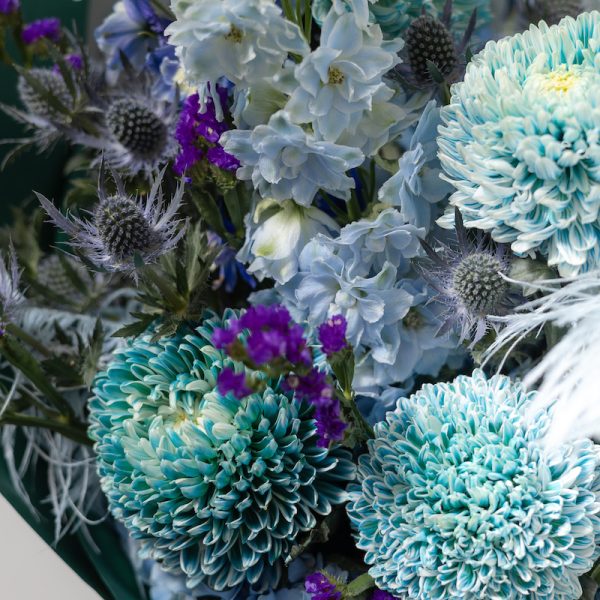 A close-up side view of the Art of Blue bouquet, showing the detail of the blue flowers and feather accents.