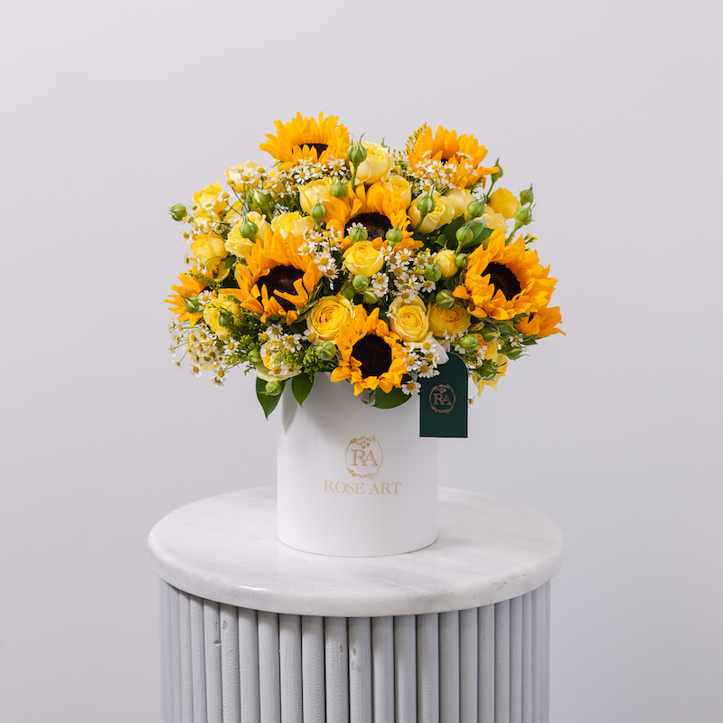 A cheerful flower box arrangement with fresh sunflowers, yellow roses, and white chamomile.