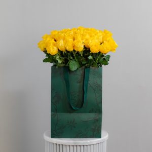 A large bunch of Yellow Armine roses arranged in a tall, elegant glass vase.